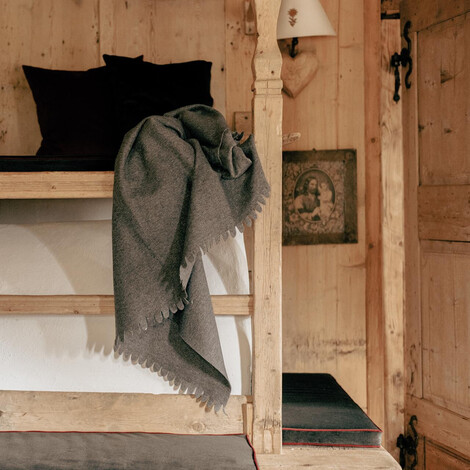 Alter Bauernofen mit rustikales Holzbett und mehreren Kissen, einer Decke und zwei Stofftieren auf der oberen Liegefläche.