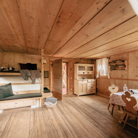 Holzverkleideter Raum mit eingebauter Sitzbank, Kissen und einem kleinen Bett mit Decken und Kuscheltieren.