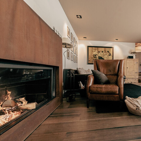Wohnzimmer mit zwei braunen Ledersesseln, einem Kamin mit Feuer, Holzboden und einem Fernseher an der Wand.