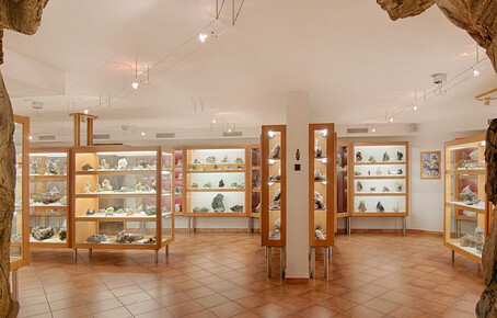 Innenraum eines Mineralienmuseums mit beleuchteten Vitrinen und Mineralienexponaten auf Fliesenboden.