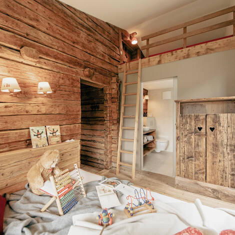 Kinderspielzimmer mit Holzverkleidung, Spielzeug, Hochbett mit Leiter und rustikalem Holzschrank mit Herz-Ausschnitten.