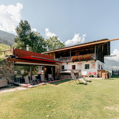 Chalet mit Terrasse, Liegestühlen und Bergwiese im Vordergrund, Berge im Hintergrund.