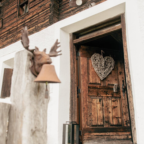 Holztür mit Herz aus geflochtenem Material und Hausnummer 14 an einer Fassade aus Holz und weißem Putz mit geschnitztem Elchkopf auf einem Pfosten davor.