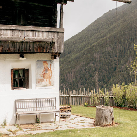 Chalet mit bemalter Fassade, zwei Holzbänken davor und Berglandschaft im Hintergrund.