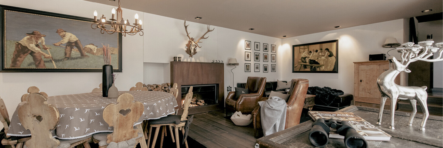 Wohnzimmer mit Holzmöbeln, Kamin, Hirschgeweih an der Wand und dekorativen Hirschfiguren auf einem Tisch.